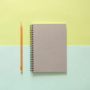 Flat lay of a spiral notebook and pencil on a pastel background, ideal for school and office themes.